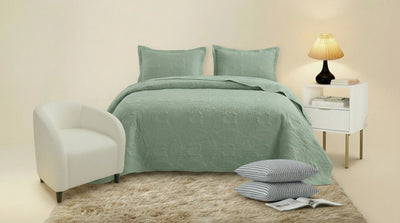 Green bedspread set on a bed with pillows and a lamp in a bedroom setting.